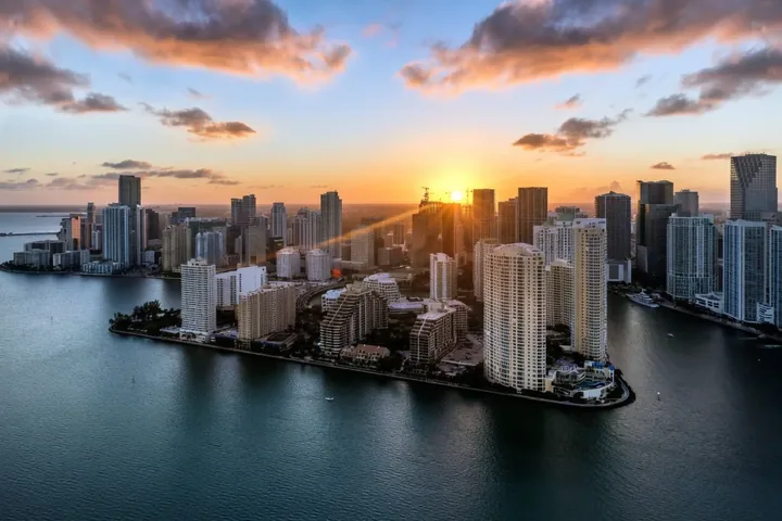 Vista aérea al atardecer de las torres de condominios frente al agua de Brickell Key, con el perfil urbano de Brickell en Miami