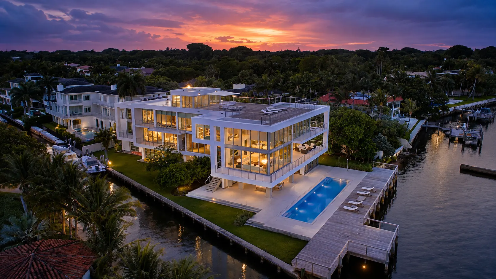 Contemporary waterfront estate in Coconut Grove at dusk with pool, dock and seawall on Biscayne Bay, surrounded by tree canopy