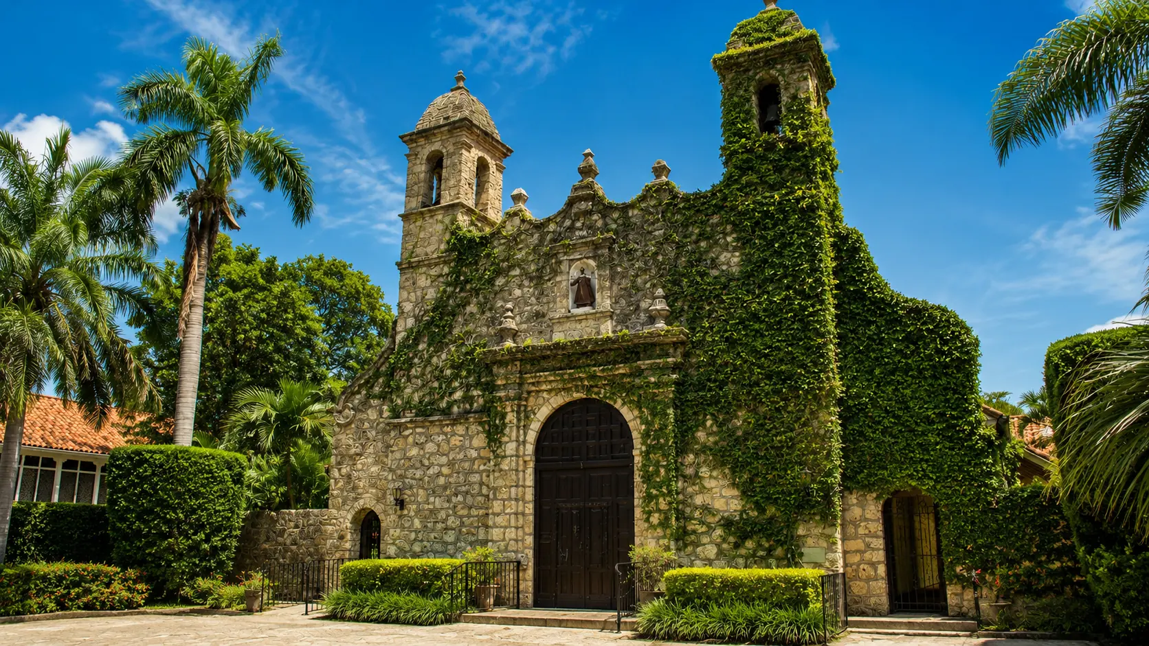 Historic coral rock building draped in ivy beneath royal palms and mature tree canopy in Coconut Grove, Miami
