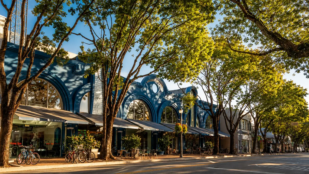 Tree-lined street in the Coconut Grove village core with arched storefronts, sidewalk cafés and dappled canopy shade