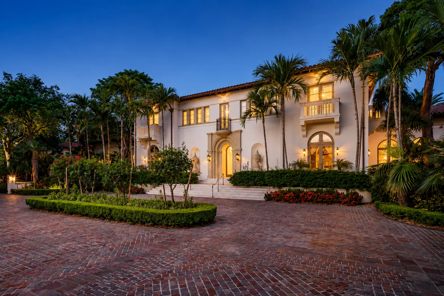 Casa de lujo de estilo mediterr&aacute;neo con patio de entrada de ladrillo y palmeras al atardecer en Coral Gables, Miami, Florida