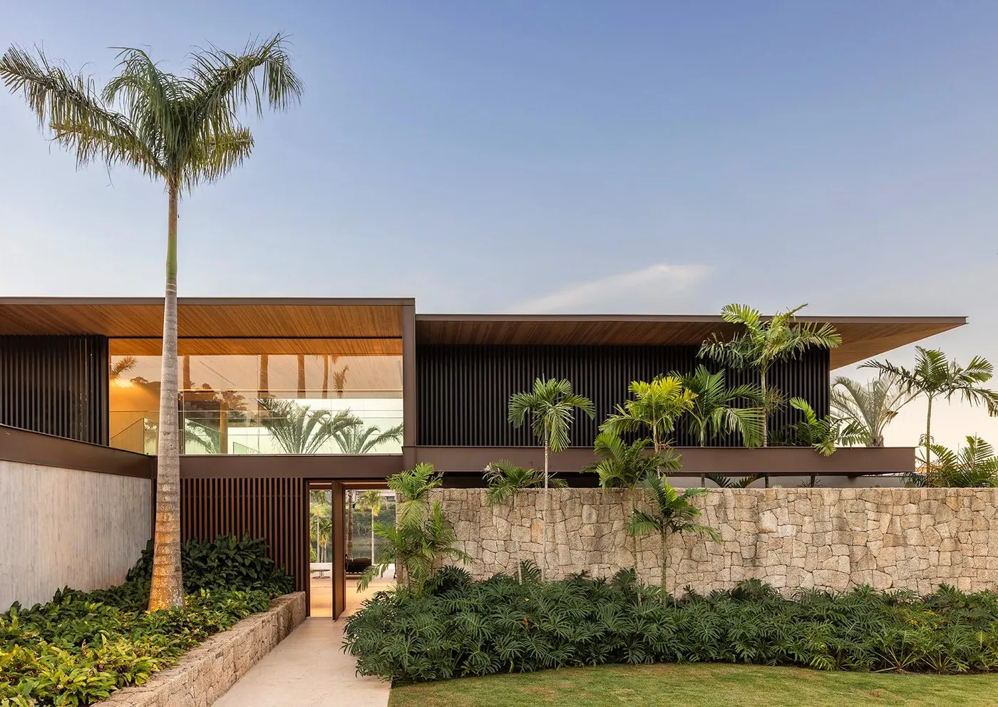 Contemporary two-storey tropical-modern residence with a cantilevered roof, wood screens, stone base wall and royal palms, representative of new custom homes in the Ponce-Davis area