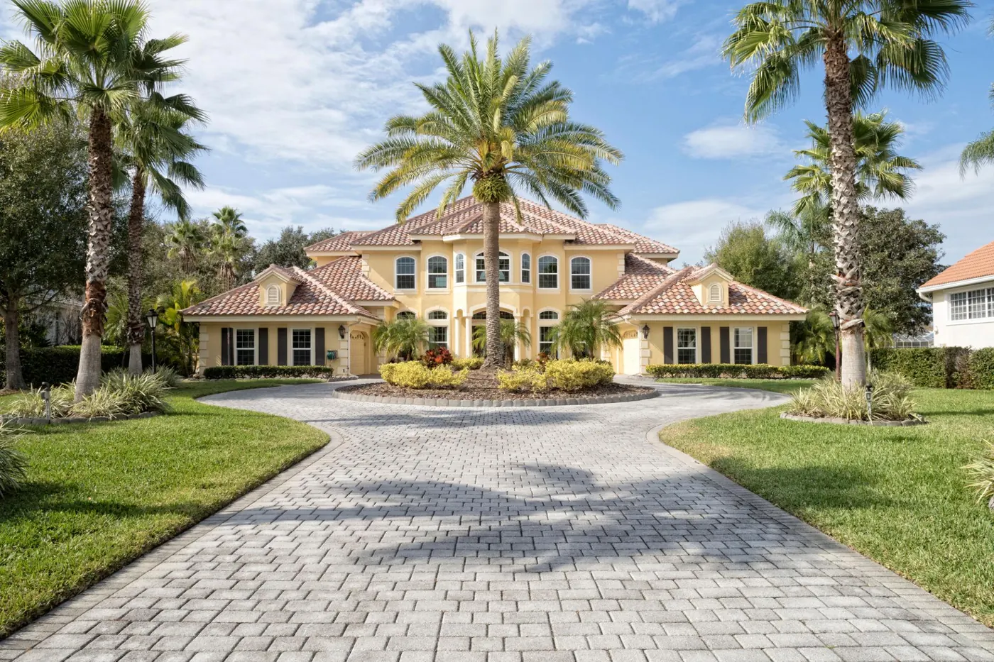 Two-storey Mediterranean-style estate with a terracotta tile roof, long paver driveway and palm-lined front lawn, representative of established luxury homes near Ponce-Davis