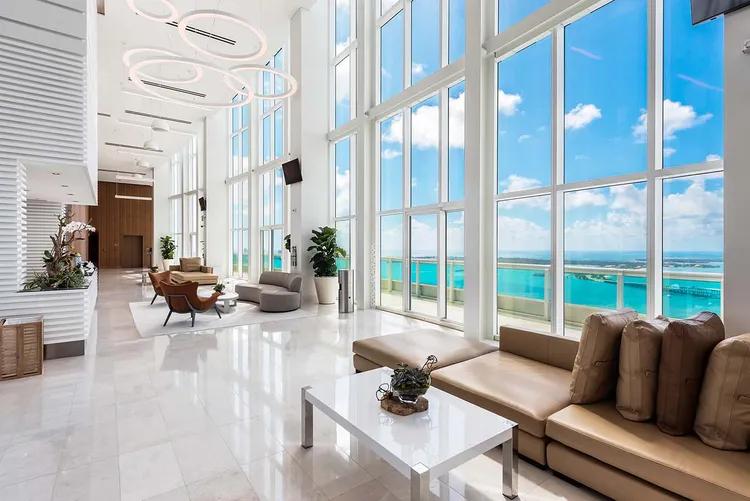 Sal&oacute;n de residentes de doble altura lleno de luz, con ventanales del piso al techo y vistas a Biscayne Bay en Santa Maria Brickell