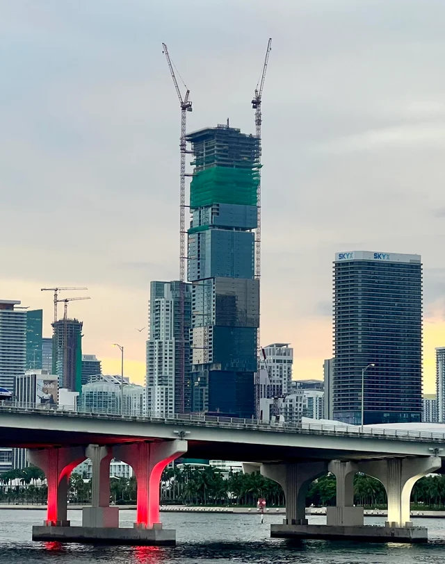 Waldorf Astoria Miami rising above the Downtown Miami skyline in August 2026, showing the stacked offset cubes with completed glass below and open structure at the top