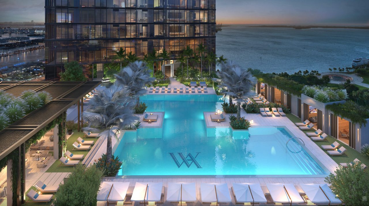 Resort pool deck with cabanas, sun loungers and palms overlooking Biscayne Bay at dusk at Waldorf Astoria Residences Miami